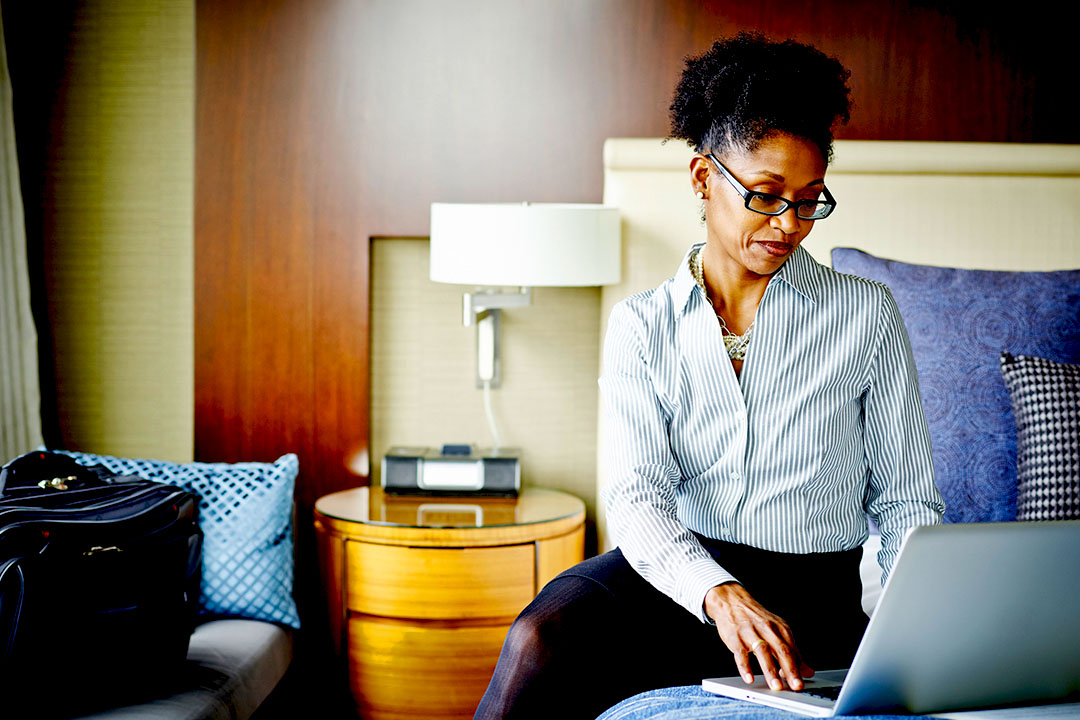 Woman sitting on hotel bed working on a laptop.