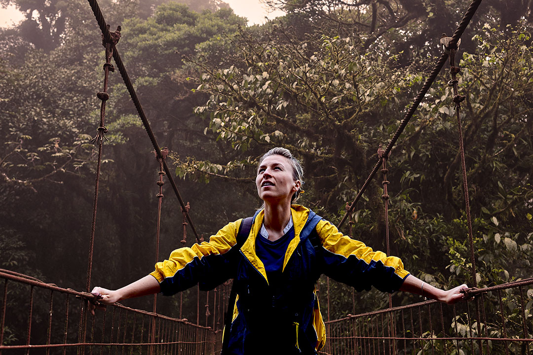 Woman walking on a rope bridge through the woods