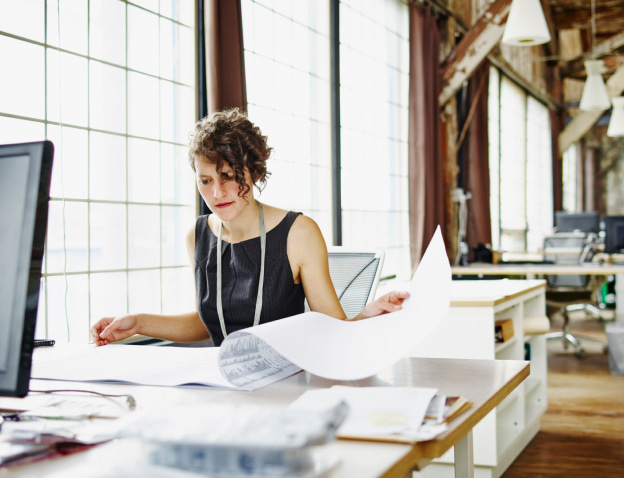 A woman in a sleeveless black dress reviews papers in a sunlit office.